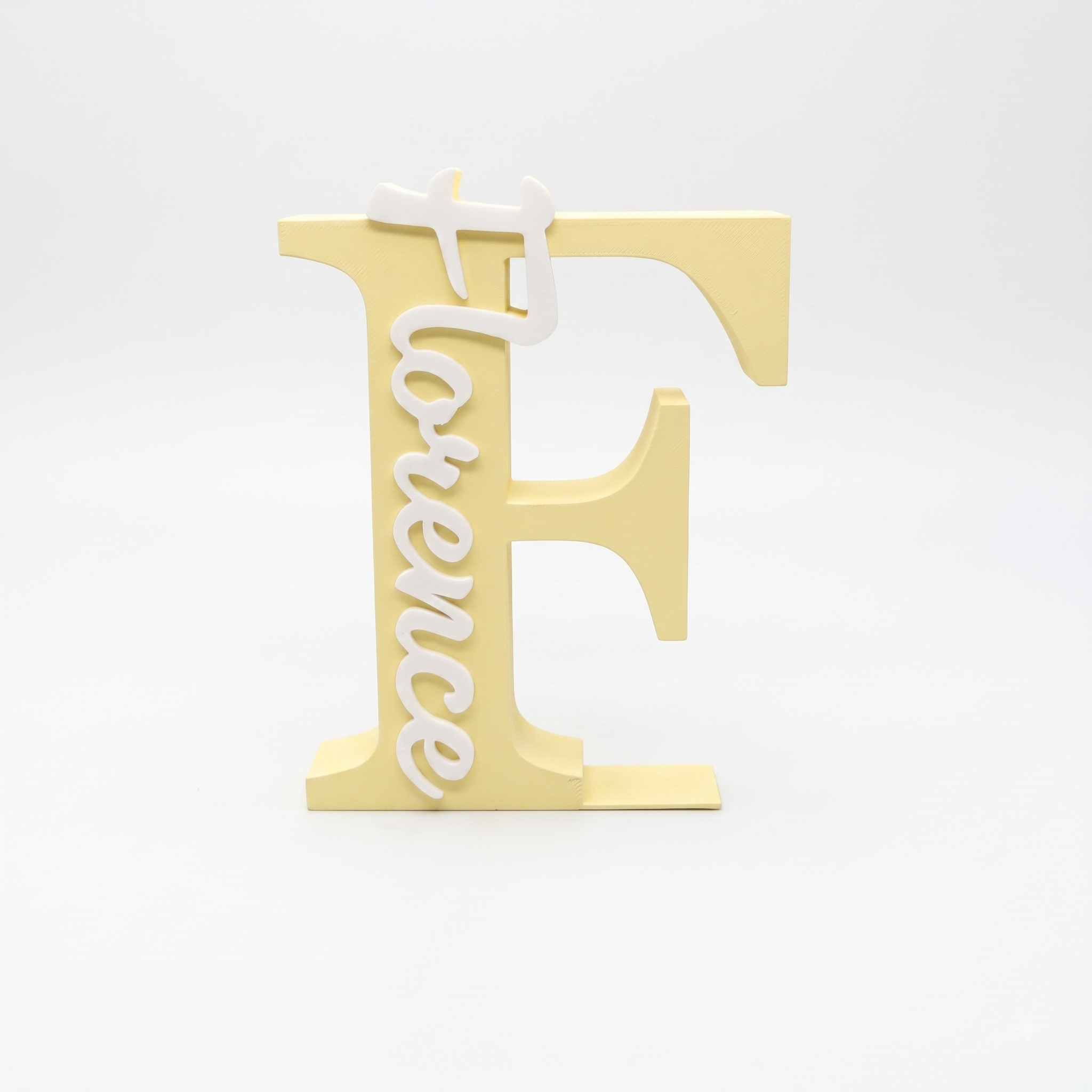A decorative freestanding letter F in pale yellow with the word 'Florence' in white script running vertically down the left side, photographed on a clean white studio background.