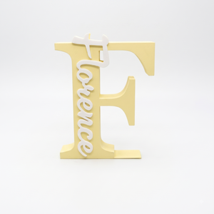 A decorative freestanding letter F in pale yellow with the word 'Florence' in white script running vertically down the left side, photographed on a clean white studio background.