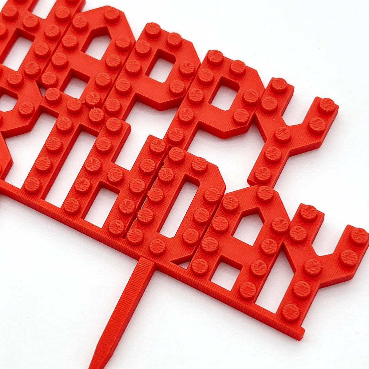Close-up of red 3D printed brick-stud Happy Birthday cake topper showing raised lettering and stud texture